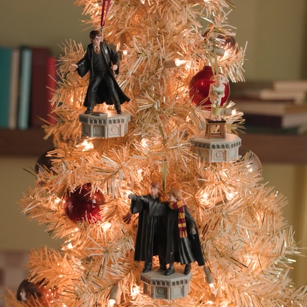 Three Keepsake Ornaments depicting moments from the movie Harry Potter and the Chamber of Secrets are hanging on a white and gold Christmas tree lit with white lights.