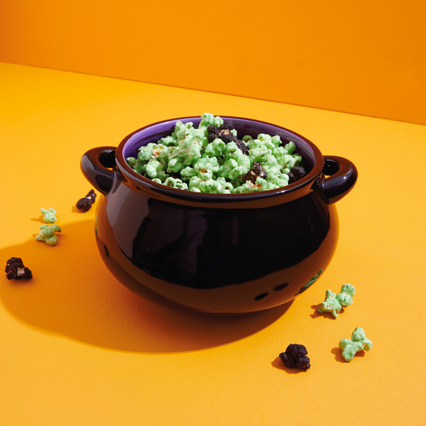 A shiny black ceramic cauldron filled with green and black candied popcorn.