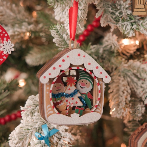 A Keepsake Ornament featuring papercraft artistry and the characters Gnaughty and Gnice hangs on a Christmas tree branch.