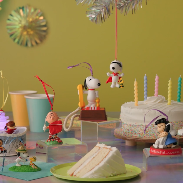 Several Keepsake Ornaments featuring characters from the Peanuts Gang, including Snoopy, Charlie Brown and Lucy, sit on a tabletop decorated for a 75th anniversary celebration.