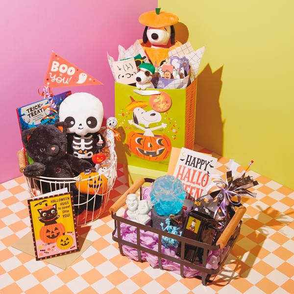 Three different themed Halloween boo bags or baskets sit on an orange and white checkered surface; themes include Peanuts Halloween, classically cute kids Halloween, and Disney The Haunted Mansion.