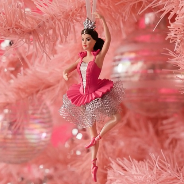 A Keepsake Ornament depicting a dark-haired Ballerina Barbie hangs from a pink Christmas tree.