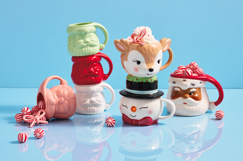 A collection of vintage-inspired Christmas mugs, including red, white, mint green and pink sculpted Santa face mugs; a sculpted mug shaped like a reindeer head; a sculpted mug shaped like a snowman in a tophat, and a sculpted mug shaped like a dark-skinned, winking Santa.