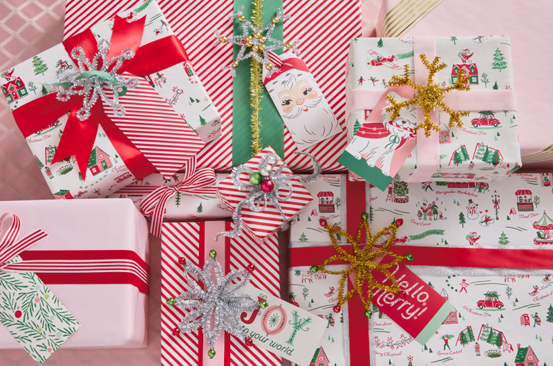 A collection of Christmas gifts wrapped in vintage-style wrap in shades of red, white and pink, with metallic pipe cleaner embellishments shaped like stars, snowflakes and wreaths.